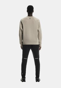 Hanorac bej cu guler rotund și mâneci raglan, asociat cu pantaloni negri cu accente reflectorizante și un design conic.