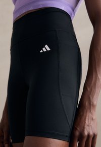 Pantaloncini sportivi neri dal design aderente con una texture liscia, caratterizzati da un logo a tre strisce bianche sul lato e un dettaglio con tasca.