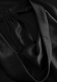 Čierna hodvábna látka s hladkým, lesklým povrchom. Materiál sa jemne spúšťa so zberaným detailom na vrchu, čím vytvára elegantné záhyby.