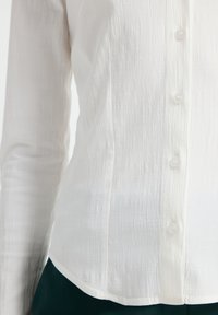 Witte button-up shirt gemaakt van textiel met textuur, voorzien van een rij kleine, ronde knopen en een licht gebogen zoom.