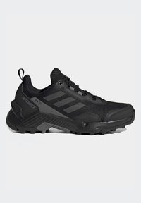 Chaussure de sport noire avec un dessus en maille texturée, un embout renforcé et une semelle à relief distinctive pour l'adhérence. Présente trois rayures en relief.