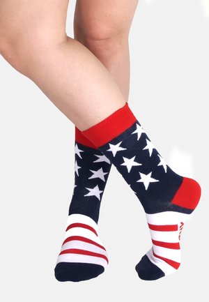 Calze di cotone con base blu navy, motivo a stelle rosse e bianche, e polsini rossi. Strisce orizzontali rosse e bianche sulle suole. Design a tema sportivo.