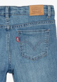 Jeans de mezclilla azul claro con una etiqueta de cuero marrón que dice "Levi Strauss & Co." y una etiqueta roja de Levi's en el bolsillo trasero.