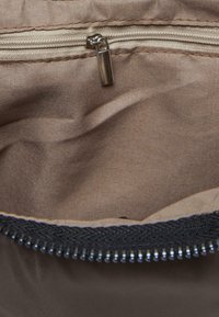 Rudas audinys krepšio viduje su sidabriniu užtrauktuku. Užtrauktukas turi tekstūruotą trauklę ir juodos spalvos pintą krašto detalę.