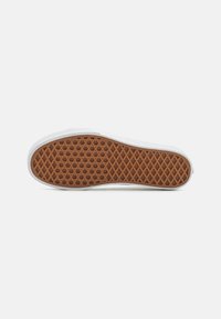 Zool van een witte sneaker met een bruin wafelprofiel, gefotografeerd op een effen witte achtergrond.