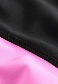Czarna i różowa tkanina o gładkiej fakturze, z wyraźnym szwem w miejscu, gdzie spotykają się dwa kolory, podkreślająca sportowy charakter.