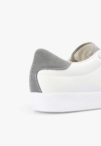 Zapatilla blanca con un talón de gamuza gris texturizada, parte superior de cuero liso y una suela de goma blanca con un patrón geométrico.