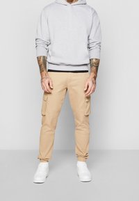 Felpa grigia con cintura nera, pantaloni cargo beige con tasche laterali e sneakers bianche. Look casual, vestibilità rilassata e design confortevole.