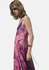 Blumenkleid im Maxistil mit tiefem Ausschnitt, das ein rosa-lila Druckmuster aufweist. Aus leichtem Stoff gefertigt, hat es eine fließende Silhouette und Spaghettiträger.