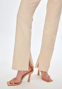 Pantalones de pierna ancha beige con aberturas laterales, combinados con sandalias de tacón nude con tiras finas y diseño de punta cuadrada.