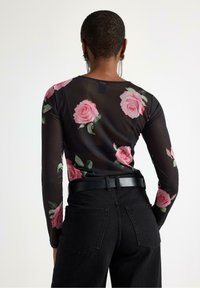 Sort gennemsigtig bluse med lange ærmer og mønster af lyserøde roser. Sammen med høj-taljede sorte jeans med en simpel kant og baglommer.