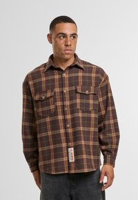 Brown and beige plaid flannel shirt with a button-up front, two chest pockets, and a sewn label at the hem. Soft texture.