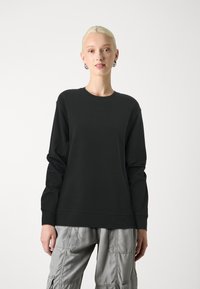 Sort sweatshirt med lange ærmer, rund halsudskæring og ribbede manchetter, kombineret med grå cargo bukser med flere lommer og en blank overflade.