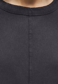 Κοντινό πλάνο μαύρου μπλουζιού με στρογγυλεμένο λαιμόκοψο και εμφανές κάθετο ράμμα που τρέχει κατά μήκος του κέντρου του υφάσματος.