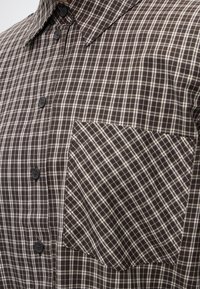 Chemise à carreaux marron et beige avec boutons, col pointu et poche poitrine avec motif à carreaux en diagonale.