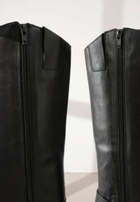 Botas de cuero negras hasta la rodilla con un diseño elegante, que cuentan con doble cremallera en los lados exteriores y una textura suave.