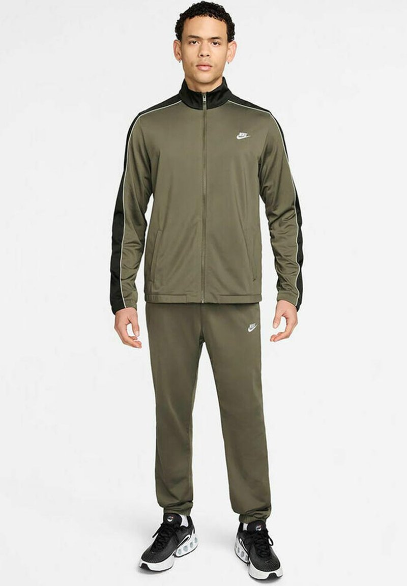 Chándal Nike de color verde oliva con acentos laterales negros, chaqueta con cremallera, pantalones con cintura elástica y un pequeño logo en el pecho y los pantalones.