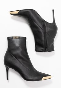 Czarne botki sięgające kostki, wykonane z gładkiego materiału, z szpiczastym noskiem z złotym akcentem, smukłym obcasem oraz bocznym zamkiem błyskawicznym.