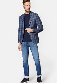 Marynarka w niebieską kratę z brązowym akcentem, zestawiona z granatowym T-shirtem, jasnoniebieskimi dżinsami i ciemnymi trampkami.