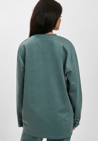Langärmliges Sweatshirt in gedämpftem Blaugrün, aus einer weichen Baumwollmischung gefertigt, mit entspannter Passform und runder Ausschnittlösung mit minimalen Nähten.