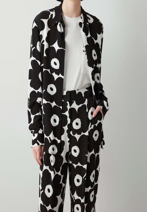Persona con camisa de patrón floral en blanco y negro y pantalones de pierna ancha a juego, combinados con una camiseta blanca lisa con cuello redondo.