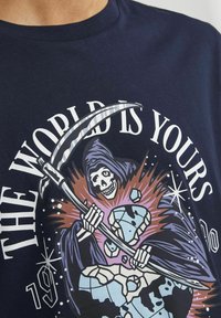 T-shirt en coton bleu marine avec un motif représentant une figure squelettique en capuche tenant une faux, accompagné du texte « LE MONDE EST À TOI. »