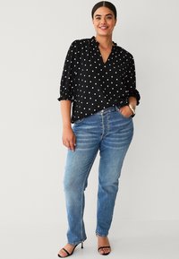 Black polka dot blouse with v-neck, puffed sleeves, and textured fabric paired with light blue straight-leg jeans and black high-heel sandals.