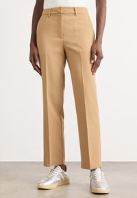 Tan tailored pants with a straight leg design, featuring a smooth texture and belt loops, paired with metallic sneakers.