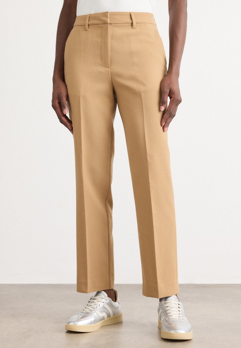 Tan tailored pants with a straight leg design, featuring a smooth texture and belt loops, paired with metallic sneakers.