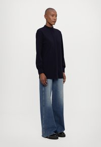 Marineblå langermet topp med høy krage, kombinert med vide, falmede denimjeans og svarte platå-sko. Jevn stofftekstur.