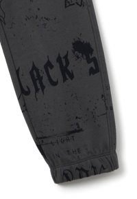 Manga de tela gris oscuro con texto gótico negro y estampado desgastado, mostrando parte de la palabra "BLACK" y puño elástico en la muñeca.