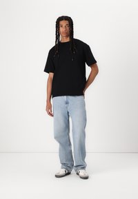 Tricou negru cu mânecă scurtă, croială lejeră. Asortat cu blugi drepți, de culoare albastră deschisă și adidași alb-negru. Estetică simplă și casual.