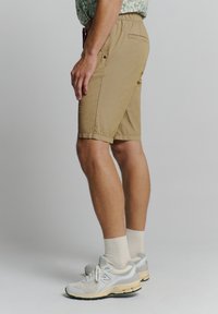 Lichtbruine, knielange shorts gemaakt van een stof met een gladde textuur, met zijzakken en een achterzak, gecombineerd met lichtgekleurde sneakers.