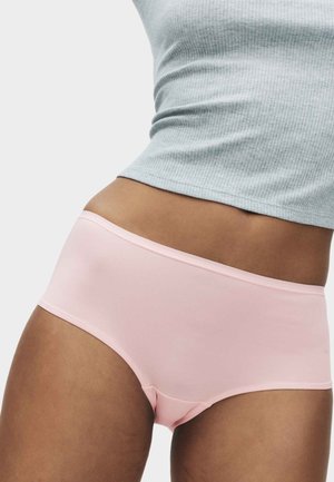 Vrouw die lichtroze naadloze onderkleding en een grijs geribbeld cropped top draagt, torso en bovenbenen zichtbaar.