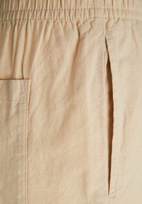 Beige tyg med en lätt struktur, med resårmidja och sidficka. Minimalistisk design med sydda detaljer.