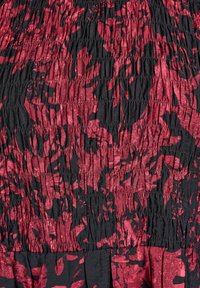 Nærbillede af sort stof med rød abstrakt blomsterprint og indsamlet elastisk shirring tekstur.