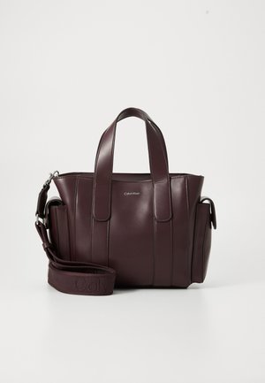 Dark burgundy leather tote handbag with dual handles, side pockets, and an adjustable shoulder strap featuring embossed branding.
