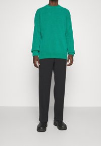 Turkos stickad tröja med rund halsringning, ribbade ärmslut och nederkant. Kombinerad med mörkgrå byxor med platt front och svarta slip-on skor.