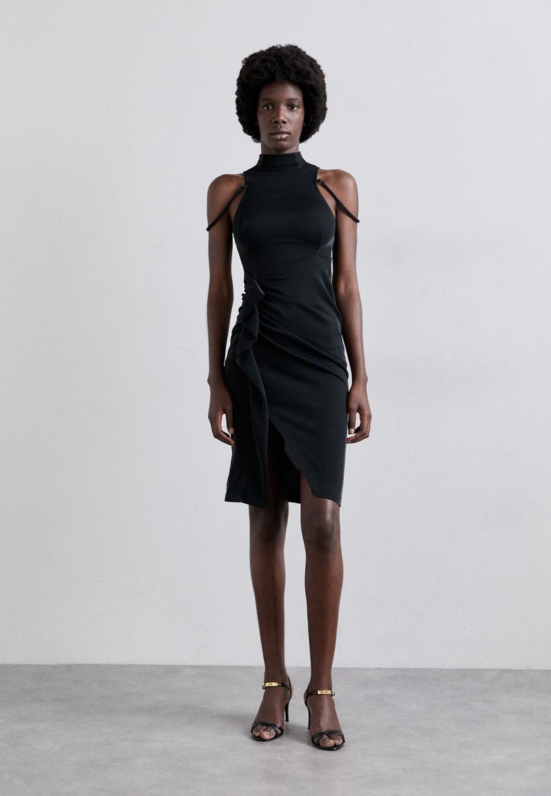 Vestido negro ajustado de cuerpo con cuello alto y hombros descubiertos. Presenta un detalle retorcido en la cintura y una abertura alta hasta el muslo. Textura suave.
