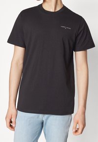 Camiseta de algodón negra con cuello redondo, mangas cortas y un pequeño logotipo blanco en el lado izquierdo del pecho. Ajuste casual con una textura suave.