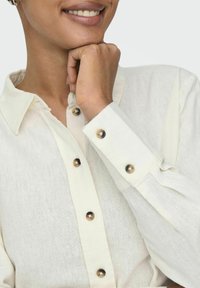 Weiße Hemdbluse aus strukturiertem Stoff, mit klassischem Kragen, sichtbaren Knöpfen an den Manschetten und lässiger Passform.