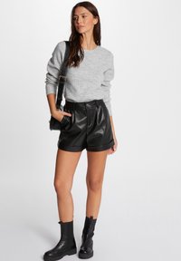 Grauer Strickpullover, schwarze Shorts aus Kunstleder mit Falten, schwarze Knöchelstiefel und eine schwarze Umhängetasche. Schlichtes, modernes Design mit subtilen Texturen.