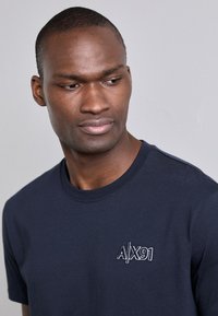 Camiseta de algodón azul oscuro con cuello redondo y mangas cortas, con un gráfico bordado "A/X91" en la parte izquierda del pecho.