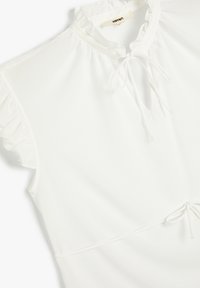 White sleeveless blouse with ruffled collar and sleeves, featuring a tie closure at the neckline and waist.