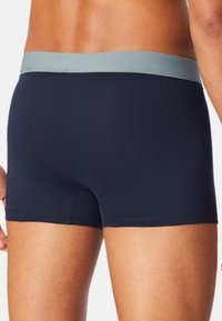 Marineblaue Boxershorts mit einem hellgrauen elastischen Bund. Hergestellt aus einem glatten, dehnbaren Gewebe. Verfügt über einen mittelhohen Schnitt und minimale Nähte.