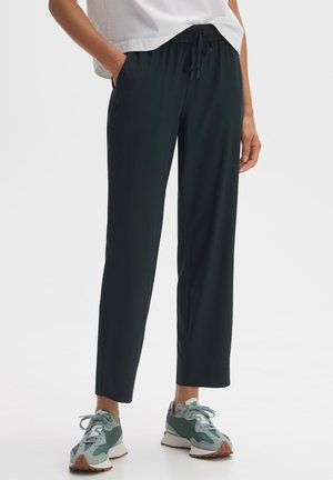 Zwarte broek met elastische tailleband en een ontspannen pasvorm, met zijzakken en een strakke textuur, gecombineerd met teal en grijze sneakers.
