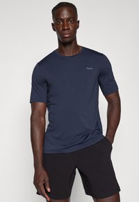 Marineblå kortærmet T-shirt lavet af blødt stof med rund hals og subtilt logodetalje på venstre bryst, i kombination med sorte shorts.