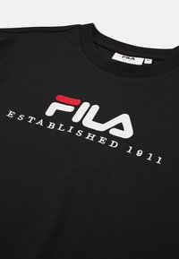 Czarna bawełniana koszulka z okrągłym dekoltem, z dużym haftowanym logo FILA w białym kolorze, z czerwonymi akcentami. Napis "ZAŁOŻONA W 1911 R."