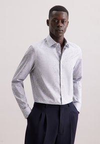 Camicia a maniche lunghe con bottoni di un blu chiaro, caratterizzata da un delicato motivo floreale, con colletto all'italiana e vestibilità su misura, abbinata a pantaloni scuri.