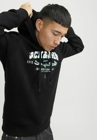 Sudadera negra con un bolsillo canguro frontal, cordón ajustable y estampado gráfico en blanco. Textura suave y dobladillo y puños acanalados.
